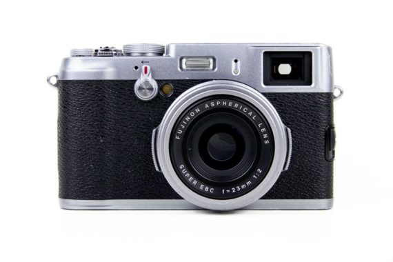 Fujifilm X100 front view featuring the silver and black version of the camera with the built-in Fujinon lens, self-timer switch and the hybrid viewfinder.