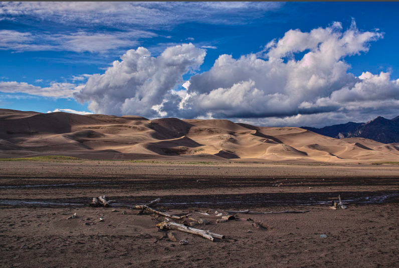 A showcase nature image featuring a desert-like area on shadowy foreground  and beautiful plain ridges of a montain wel lit by the sun in the background.